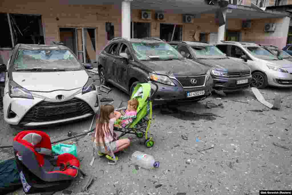 A young child keeps watch on another near damaged cars. &quot;We hear voices, people are under the rubble,&quot; Klitschko said.