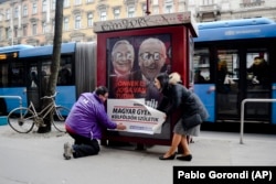 Katalin Cseh (right) of the Momentum opposition party helps to place a sticker saying: "Every sixth Hungarian child is born abroad. Let's not hand over our future," over a Hungarian government poster targeting then-European Commission President Jean-Claude Juncker and Hungarian-American financier George Soros in Budapest in February 2019.
