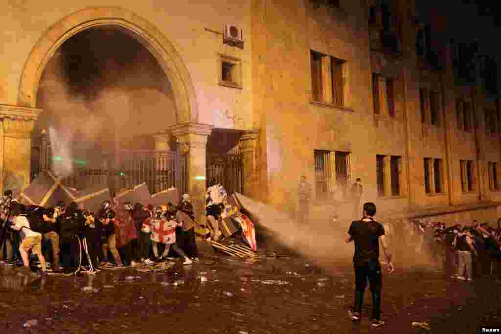 Policija ispaljuje vodeni top na demonstrante koji pokušavaju da probiju kapiju i uđu u zgradu parlamenta, Tbilisi, 1. maja 2024. Nacrt zakona predviđa da organizacije koje dobijaju više od 20 posto sredstava iz inostranstva budu registrovane kao &quot;strani agenti&quot; ili će se suočiti sa novčanim kaznama. &nbsp;