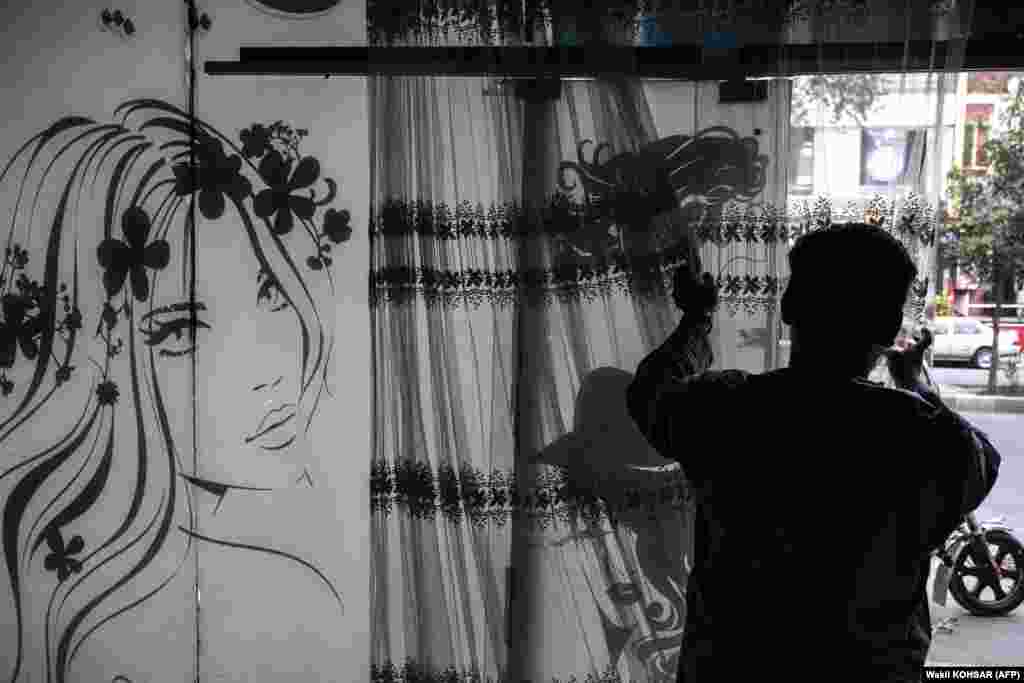 An Afghan man removes curtains inside a beauty parlor in Kabul on July 25. The Taliban ordered beauty parlors across the country to shut by the end of the month.&nbsp;