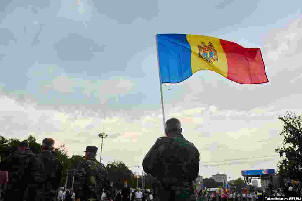 Un bărbat în uniformă militară ține steagul R. Moldova.