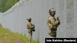 Latvian border guard officers patrol along the fence along the Latvia-Belarus border near Robeznieki, Latvia, on August 8.