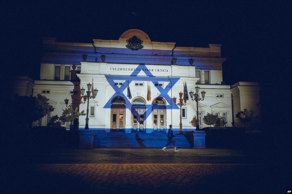 Një person duke kaluar para ndërtesës së Parlamentit bullgar në Sofje, ku është shfaqur me projektor flamuri i Izraelit, të dielën më 8 tetor 2023, për të treguar mbështetjen për Izraelin pasi&nbsp; militantët palestinezë të Hamasit&nbsp;sulmuan papritur Izraelin nga Rripi i Gazës.