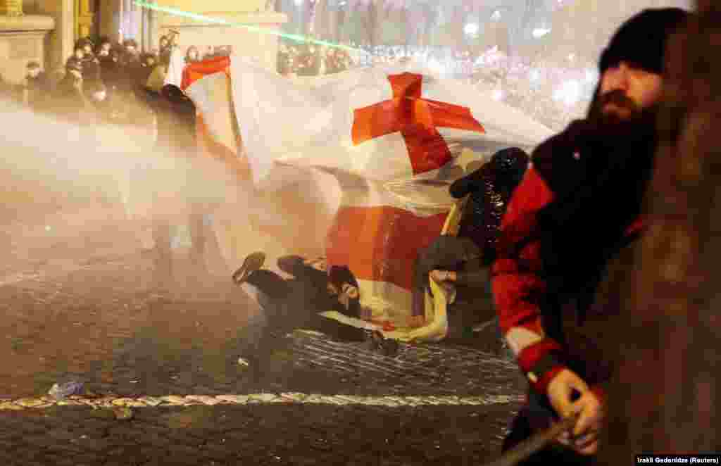 Un protestatar este pus la pământ de un tun de apă pe o stradă care duce la intrarea din spate a parlamentului.