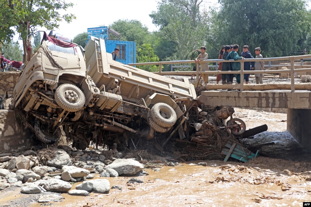 I ragazzi afgani guardano un camion che è stato investito dalle inondazioni nel distretto di Jalrez della provincia.  Shafiullah Rahimi, portavoce del Ministero per la gestione dei disastri talebani, ha dichiarato il 23 luglio che almeno 41 persone erano disperse e almeno 74 persone sono rimaste ferite.