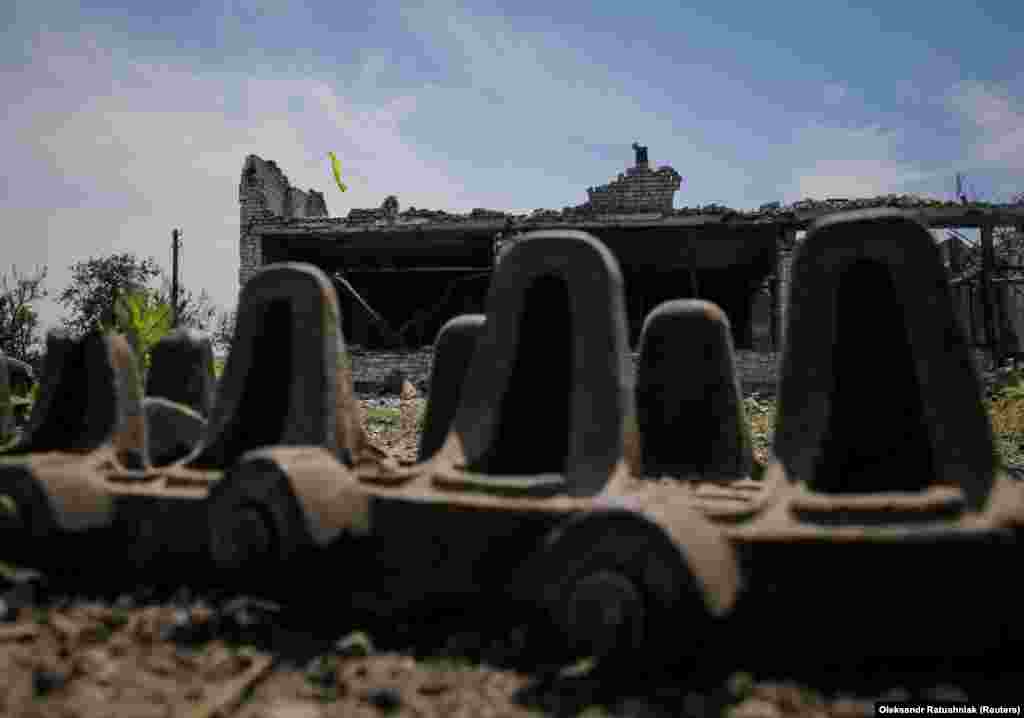 Tank tread lies on the ground near where Ukrainian soldiers placed their national flag atop a damaged home.