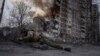 A Ukrainian police officer takes cover in front of a burning building that was hit in a Russian air strike in Avdiyivka on March 17