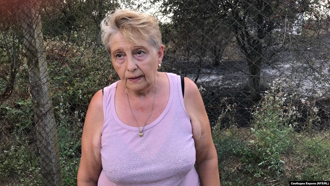Боряна, жителка на с. Отец Паисиево, е застанала до оградата на двора си, зад която се вижда пепелта от огъня, стигнал на сантиметри от къщата ѝ.