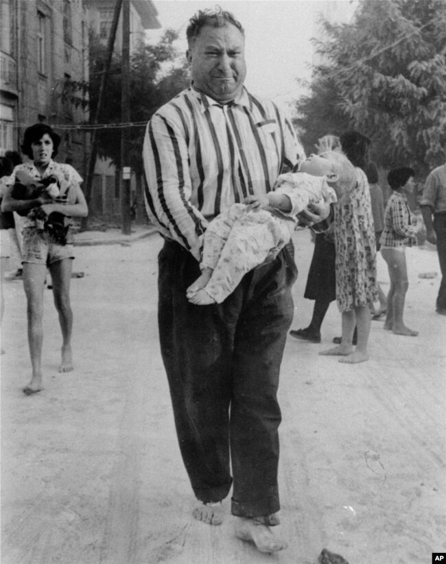 Një burrë, këmbëzbathur dhe duke qarë, mban fëmijën e tij që po vdes nëpër rrugët e Shkupit, gjatë tërmetit që vrau qindra njerëz më 26 korrik 1963. Kjo është një foto nga seria e fotografive të fotografit Sam Nocella, nga Willow Grove, PA. Nocella dhe gruaja e tij ishin në një hotel në Shkup kur ndodhi tërmeti.