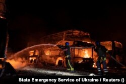 Пожарные работают на месте стоянки автомобилей, поврежденных остатками российских ракет, которые были сбиты украинской ПВО. Киев, 16 мая 2023 года