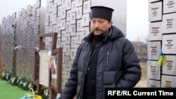 Священник Андрій Галавін біля меморіалу із іменами убитих російськими окупнатами жителів Бучі. Березень 2024 року