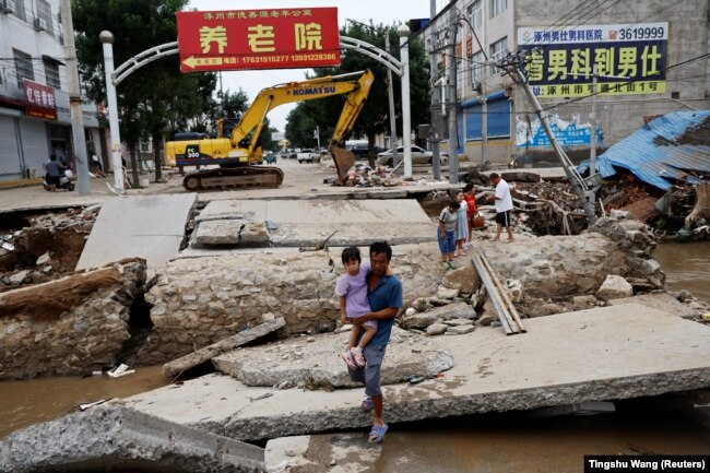 Një burrë me një fëmijë në krahë duke ecur nëpër një urë të dëmtuar pas shirave dhe përmbytjeve në Zhuozhou, provinca Hebei, Kinë, 7 gusht 2023.