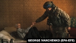 Украински полицай помага на 84-годишния Виктор, който е с увреждания, да се евакуира от териториите, граничещи с Русия, в град Вовчанск, Харковска област.