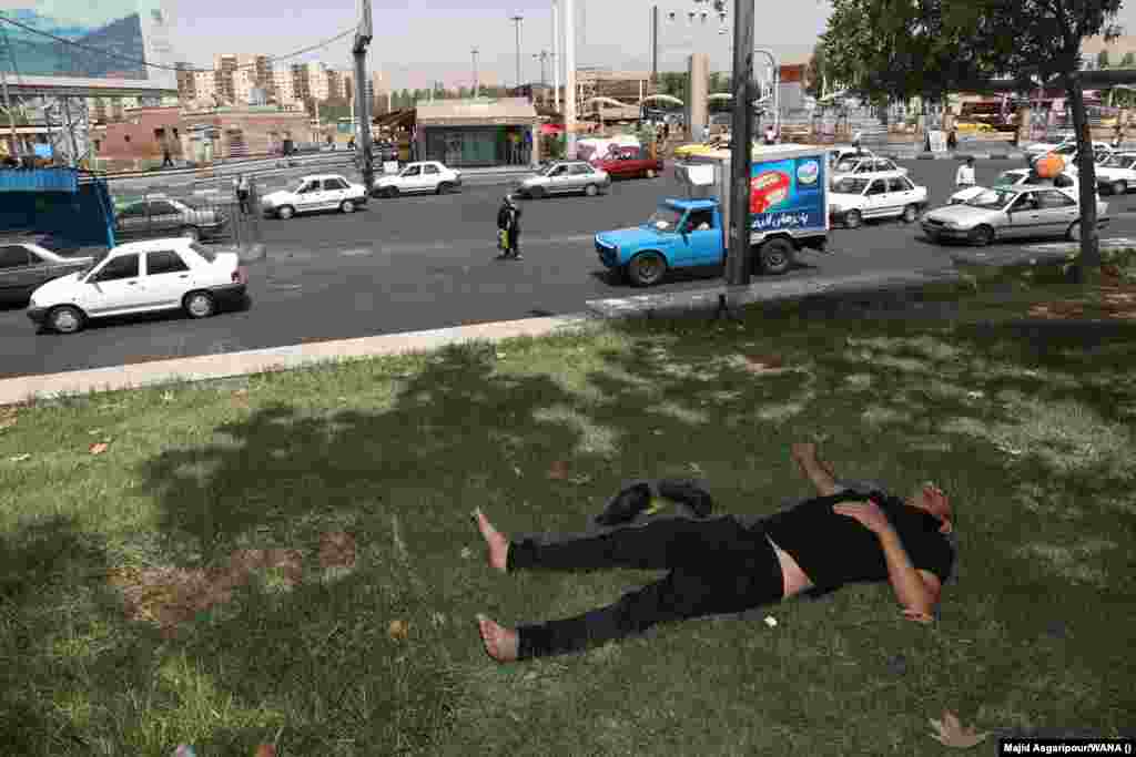 A man rests in the shade near a busy road in Tehran. The Health Ministry also warned that the two-day shutdown may need to be extended to protect people&rsquo;s health.