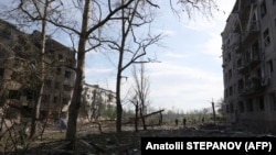 Люди стоять між будинками, які були зруйновані артилерійським обстрілом і авіаударами в Очеретиному неподалік від Авдіївки Донецької області, 15 квітня 2024 року