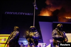 Российские правоохранители стоят в оцеплении возле горящего концертного зала «Крокус Сити Холл» под Москвой, 22 марта 2024 года