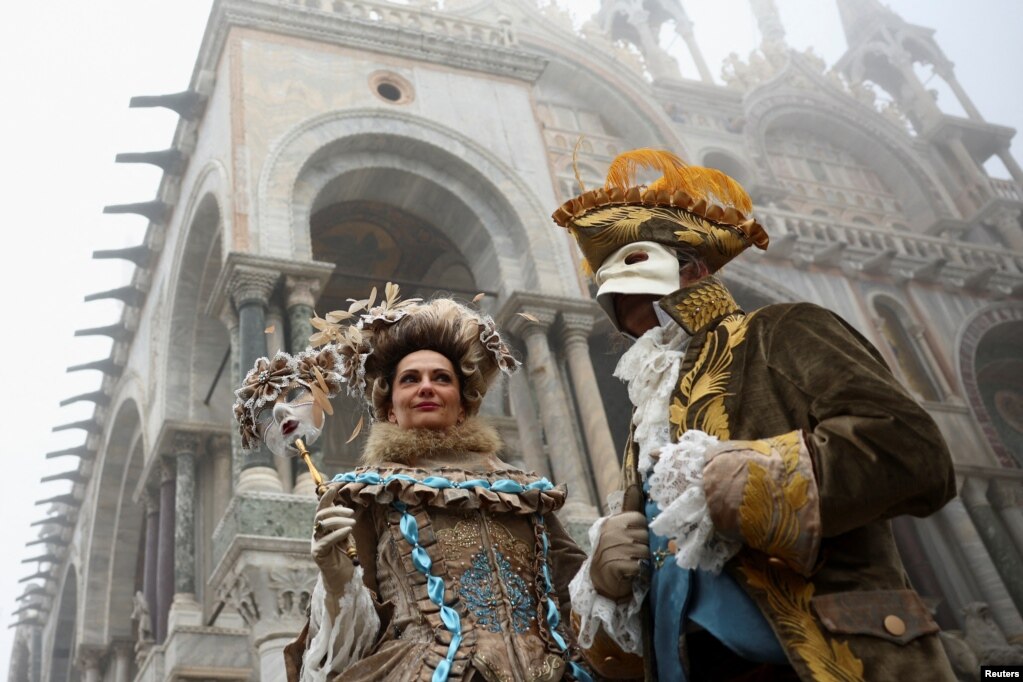 Një grua largon maskën nga fytyra, pranë një&nbsp; burri po ashtu të veshur me kostume aristokratësh gjatë Karnavalit të Venedikut.