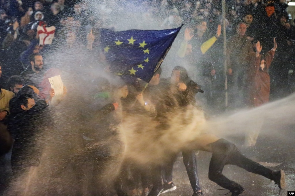 Protestuesit që mbajnë flamurin e Bashkimit Evropian goditen nga topa uji gjatë përplasjeve me policinë pranë Parlamentit të Gjeorgjisë, në Tbilisi, më 7 mars 2023. Policia gjeorgjiane përdori gaz lotsjellës dhe topa uji kundër kundër mijëra demonstruesve që dolën në rrugë në kryeqytetin Tbilisi për të kundërshtuar një projektligj të diskutueshëm të &quot;agjentëve të huaj&quot;.&nbsp;