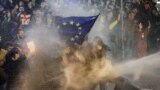 Protesters brandishing a European Union flag are sprayed by a water cannon during clashes with riot police near the Georgian parliament in Tbilisi on March 7, 2023.