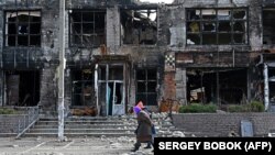 Місцеві жителі йдуть перед зруйнованим через російську агресію магазином у селі Циркуни Харківської області. Фото архівне
