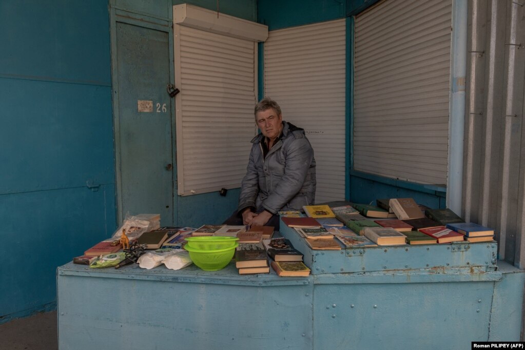 Un uomo vende libri al mercato.  Le forze di Mosca continuano a rendere la vita miserabile ai residenti di Kherson e dei villaggi vicini, che stanno subendo interruzioni di corrente e un’economia gravemente colpita dalla guerra.
