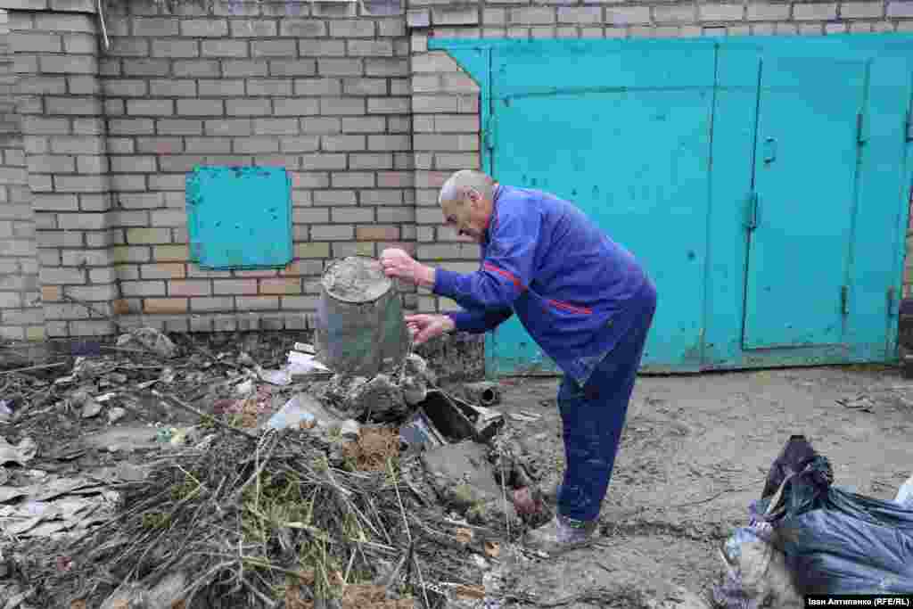 Mykola, a resident of the village of Bilozerka, empties a pail of debris from his home that was under water and is now covered in thick muck. His daughter was killed in their home by shelling a few months ago.