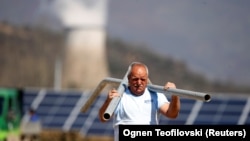 Osoba radi u blizini solarne elektrane nasuprot elektrane na ugljen u Oslomeju, Sjeverna Makedonija, 14. aprila 2022. 