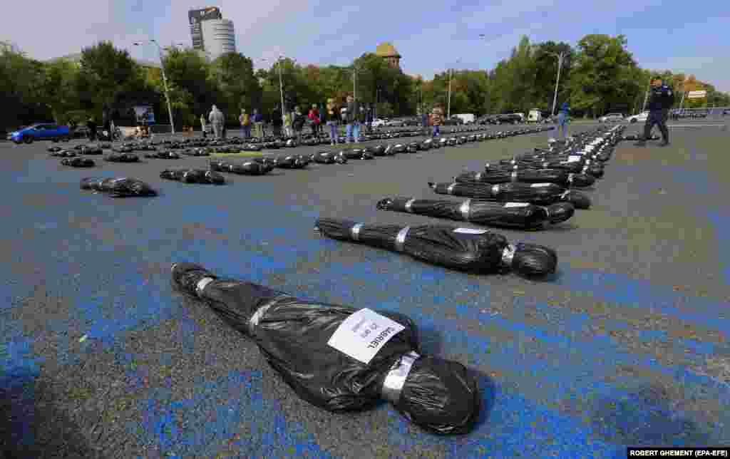 Manechine învelite în pachete de plastic, purtând etichete cu nume, vârste și locuri de muncă fictive, sunt așezate pe jos în timpul unui protest privind politicile de sănătate ale guvernului român cu privire la bolnavii de cancer, desfășurat în fața sediului guvernului din București, pe 17 octombrie.