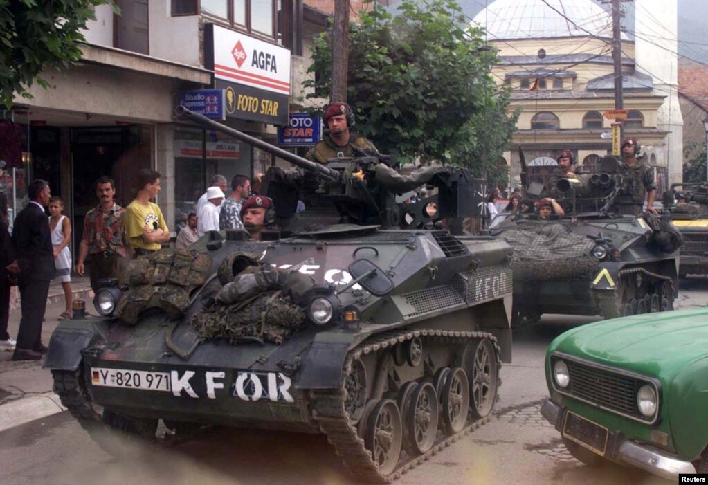 Prizren 16 korrik 1999: Mjete ushtarake gjermane shihen duke patrulluar në rrugët e Prizrenit më 16 korrik të vitit 1999. Trupat gjermane ishin vendosur atëkohë në Prizren në kuadër të misionit paqeruajtës të NATO-s.   5 qershor 2024: Kjo rrugë ka ndryshuar shumë pak. Xhamia mbetet e njëjta dhe shtëpitë përreth kanë pësuar pak ndryshime përgjatë 25 vjetëve. Disa biznese i kanë mbijetuar kohës dhe mbajnë emrin e njëjtë. 