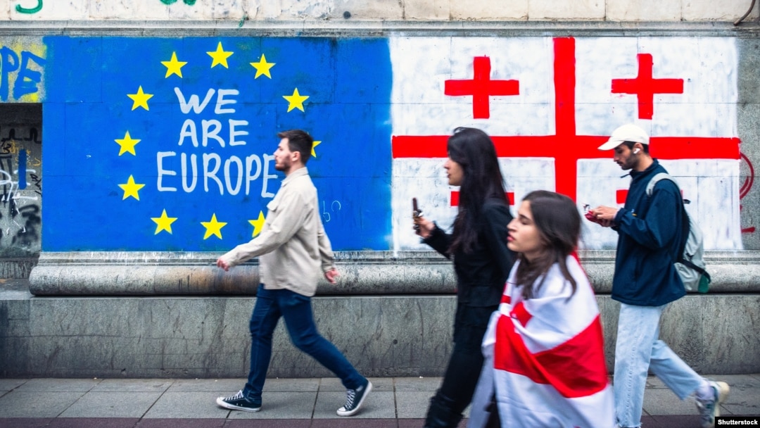 People walk past Georgian and EU flags painted on the wall in Tbilisi.