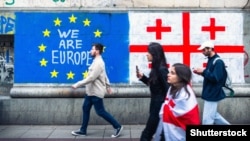 People walk past Georgian and EU flags painted on the wall in Tbilisi.