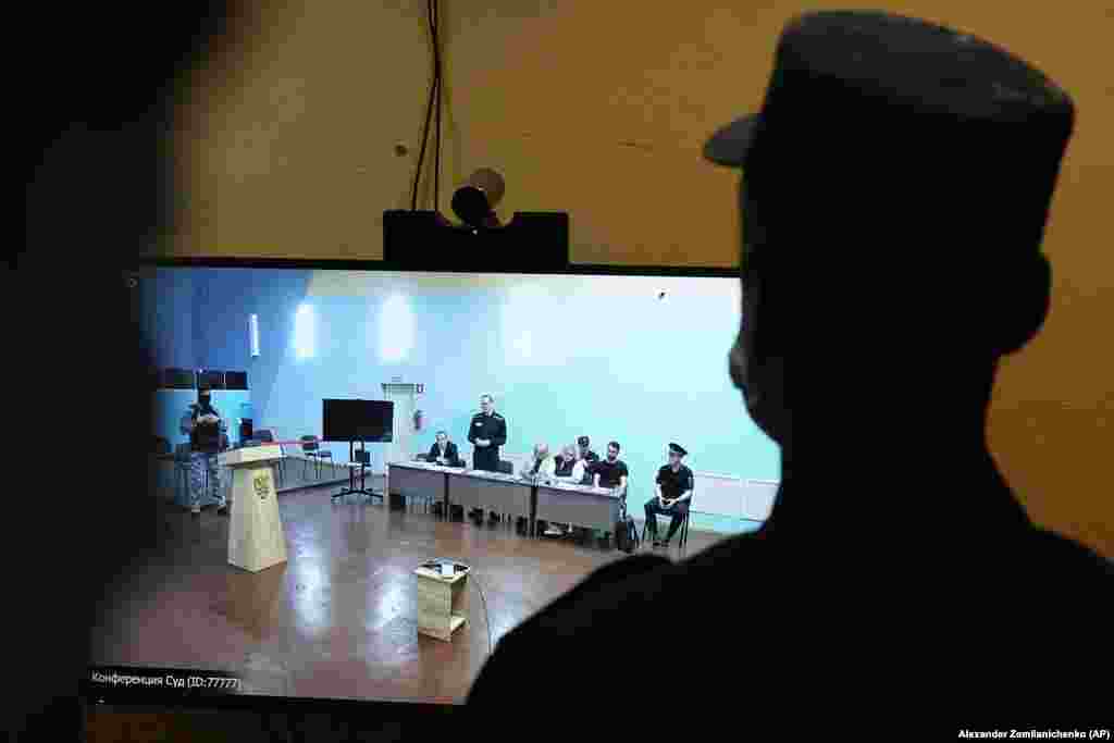 A Russian security officer stands in front of a TV screen showing opposition leader Aleksei Navalny (standing) at his widely criticized closed-door trial on extremism charges.&nbsp;
