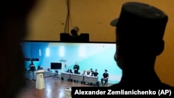 A video screen shows Aleksei Navalny (standing) speaking between his lawyers in a courtroom via video link provided by the Russian Federal Penitentiary Service on June 19.