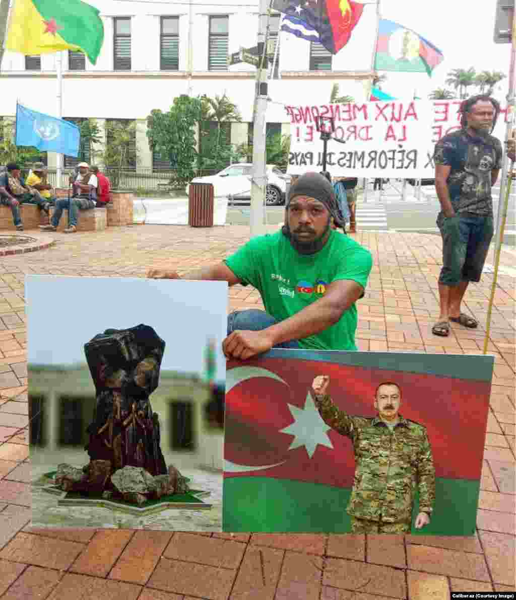 Демонстрант во Нумеа е фотографиран во март како држи слики од азербејџанскиот претседател Илхам Алиев и од азербејџанскиот воен споменик. Споменикот на сликата неодамна беше откриен во повторно преземената област Калбачар во Азербејџан. &nbsp;