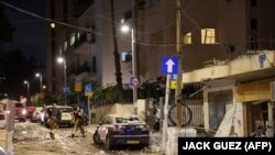 Az izraeli biztonsági erők tagjai Tel-Avivban egy törmelékekkel teli utcán, amelyet 2023. október 7-én a Gázai övezetből kilőtt rakéta talált el