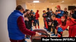 Volunteers dressed in superhero costumes greet a young cancer patient.