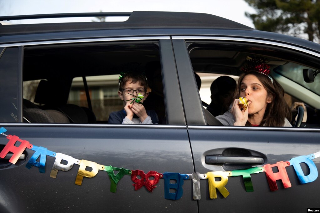 Dana Baer dhe djali i saj Jacob Baer i urojnë Avery Slutskyt ditëlindjen e gjashtë nga makina e tyre gjatë festimit të ditëlindjes me makinë, duke ruajtur distancën mes vete në West Bloomfield Township, Michigan, SHBA, 24 mars 2020.