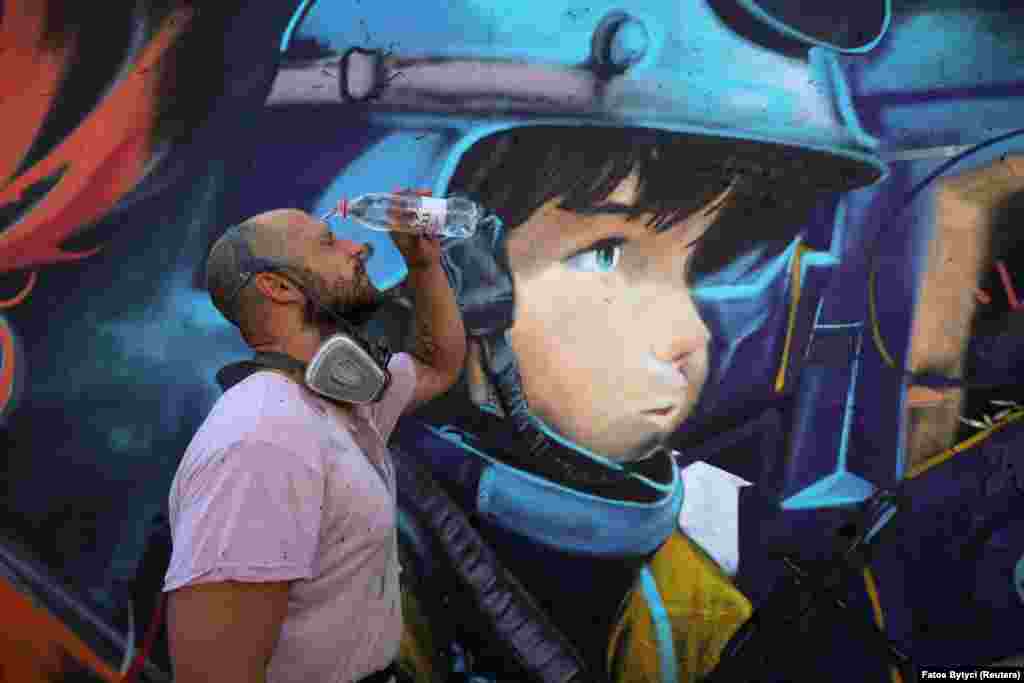 Davide Pianta, a graffiti artist from Italy, cools himself with water in front of his mural. Pristina experienced a surge in construction following the end of the Kosovo War in 1999, though more than 70 percent of all homes and apartments were built without official approval.&nbsp;
