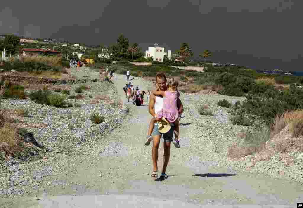 Muškarac s djetetom napušta područje koje je zahvatio požar na turističkom otoku Rodosu. 22. juli 203.&nbsp;