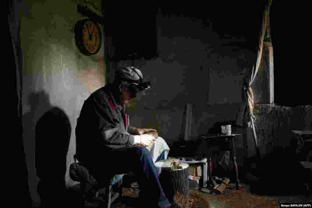 Grozdov&#39;s neighbor, 63-year-old Vitaliy Zemin, sits in the cellar, where he lives with his wife. He spends much of his time carving wooden animals while wearing a head torch.