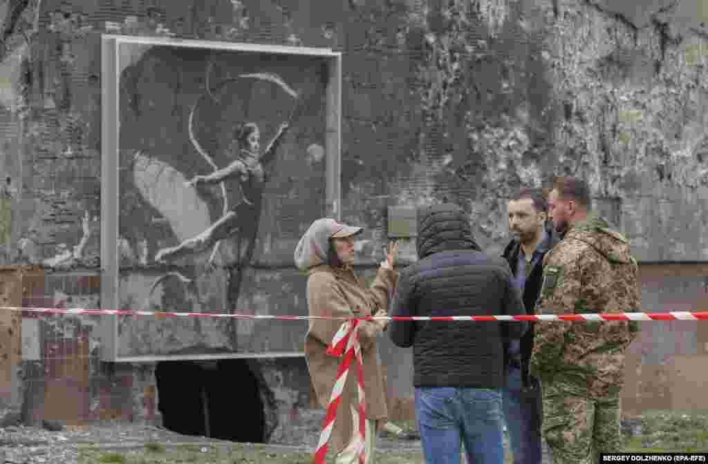 People stand next to a Banksy mural on a damaged building about to be demolished in Irpin, near Kyiv. The two residential buildings were set to be demolished after being damaged by shelling. A section of one of the two buildings, with a mural created by British street artist Banksy, will be preserved.