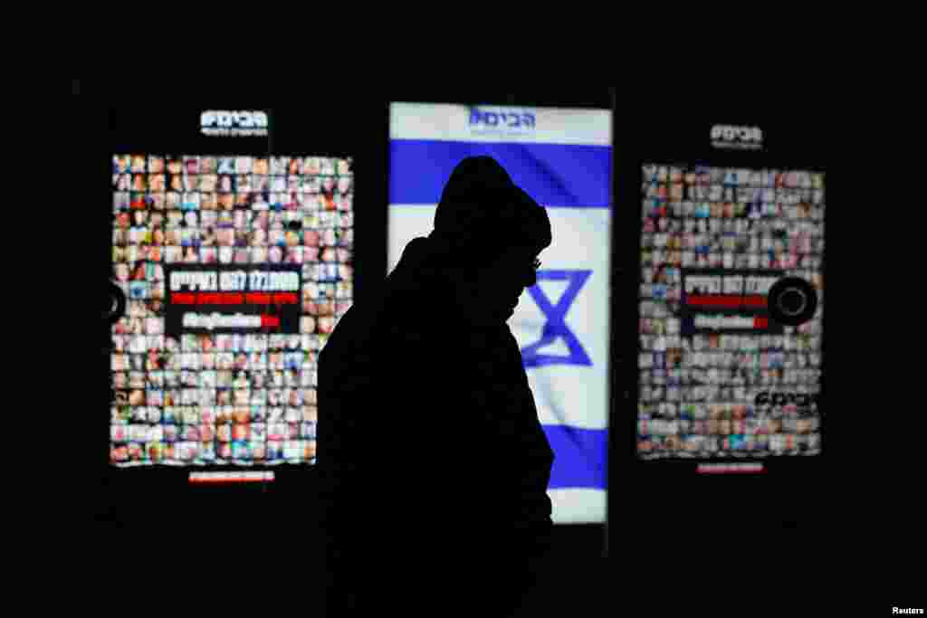 Një burrë kalon pranë ekraneve që shfaqin flamurin izraelit dhe fotografitë e pengjeve që u rrëmbyen në sulmin vdekjeprurës të 7 tetorit 2023 në Izrael nga grupi ekstremist palestinez, Hamas. Sheshi Habima në Tel Aviv, Izrael, 4 shkurt 2024.