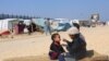 Një vajzë e zhvendosur palestineze duke e ushqyer vëllain e saj në një tendë, në qytetin jugor të Gazës, Rafah.