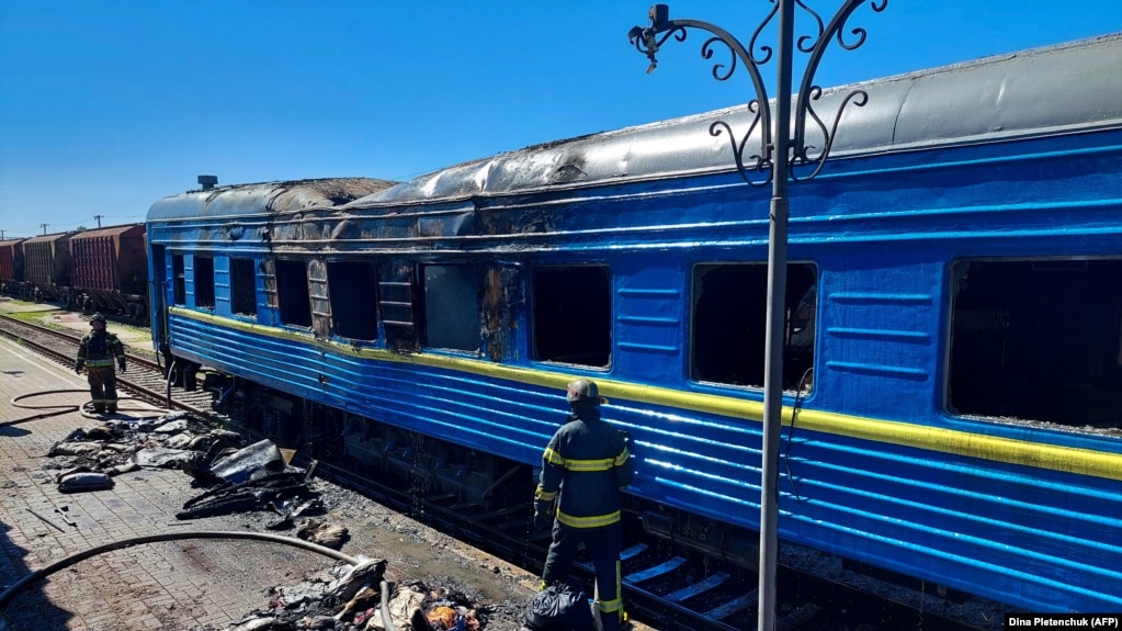 Пожежники стоять перед вагоном пасажирського потяга, пошкодженого внаслідок російського удару по Херсону, 3 травня 2023 року