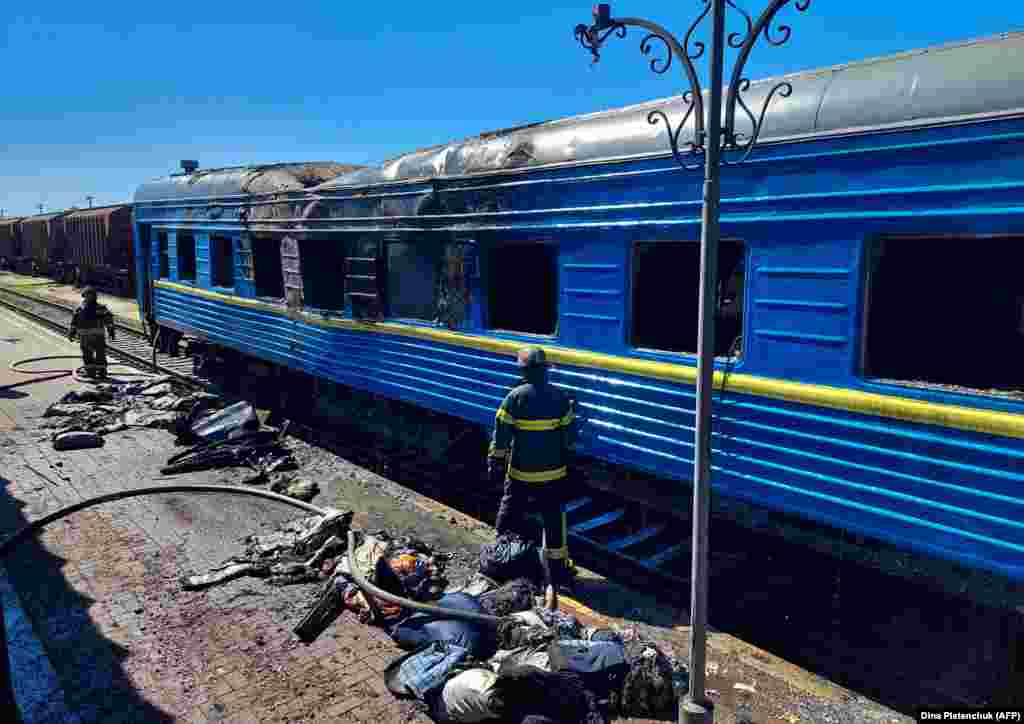 Пожежники стоять перед вагоном пасажирського потягу, пошкодженого внаслідок російського удару по Херсону, 3 травня 2023 року