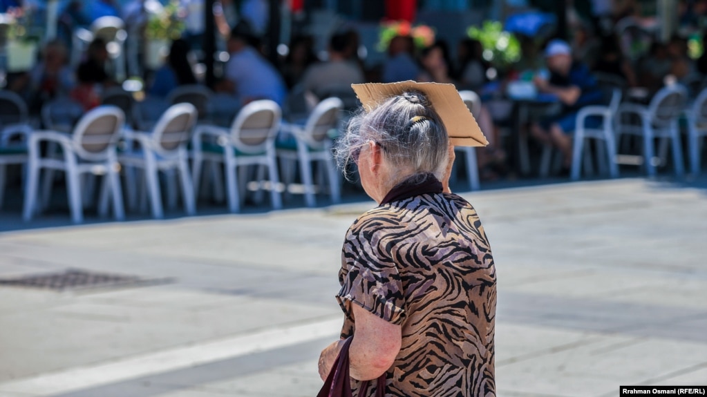 Një e moshuar mbrohet nga dielli&nbsp;përvëlues duke e mbajtur mbi kokë një copëz kartoni. 18 korrik 2023.