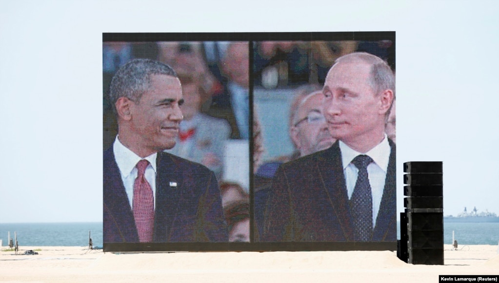 Një ekran i madh tregon presidentin e atëhershëm të SHBA-së, Barack Obama, dhe presidenti rus, Vladimir Putin, ndërsa mbërrijnë për përkujtimet e Ditës D më 2014. Fjalimi i presidentit Obama nënvizoi rëndësinë e NATO-s dhe sigurisë kolektive mes rritjes së tensioneve me Rusinë në lidhje me Ukrainën. &nbsp;