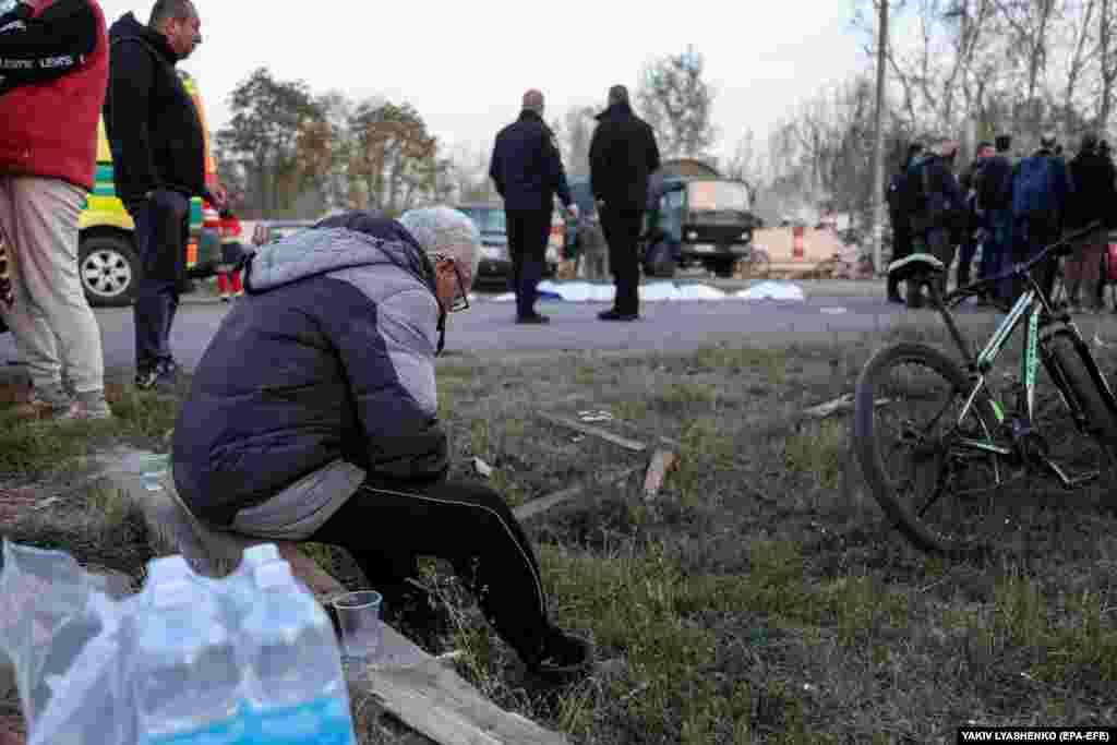 An elderly man sits alone as bodies of those killed are covered in plastic.