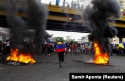 Demonstrant trči sa nacionalnom zastavom Venecuele između zapaljenih barikada tokom protesta protiv izbornih rezultata, u Puerto La Kruzu, Venecuela, 29. jula 2024.