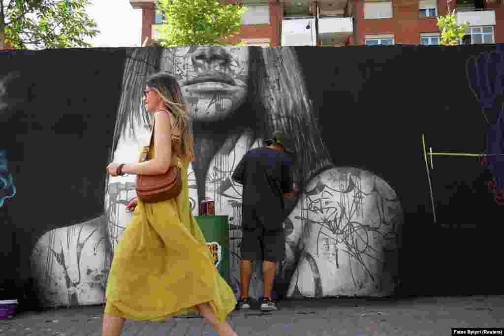 A woman walks by as Swalt, a graffiti artist from Switzerland, creates his new mural.